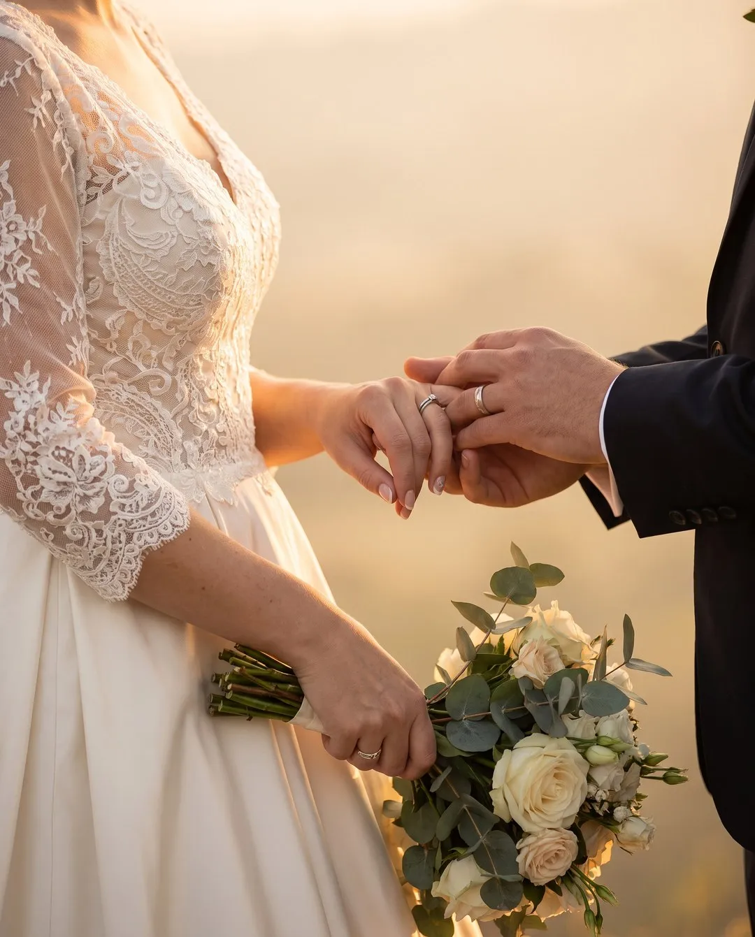 Les mains des mariés et le bouquet, dans une lumière chaude